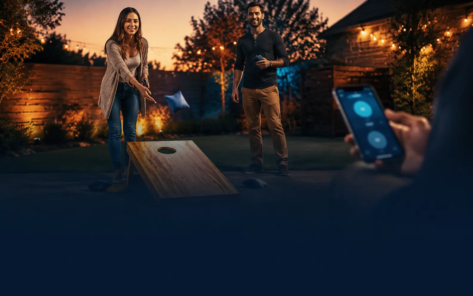 Friends playing a casual cornhole game while using a phone scoreboard